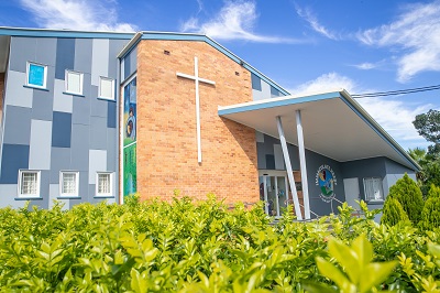 school building with brick facade, cross feature and Immaculate Heart signage surrounded by greenery