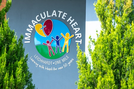 Immaculate Heart Catholic Primary School logo displayed on building wall surrounded by garden landscaping
