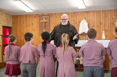students attending parish liturgy with priest speaking at altar in church setting